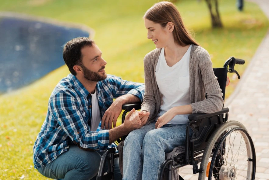 Disabled woman in wheelchair outside in park holding hand of loved one